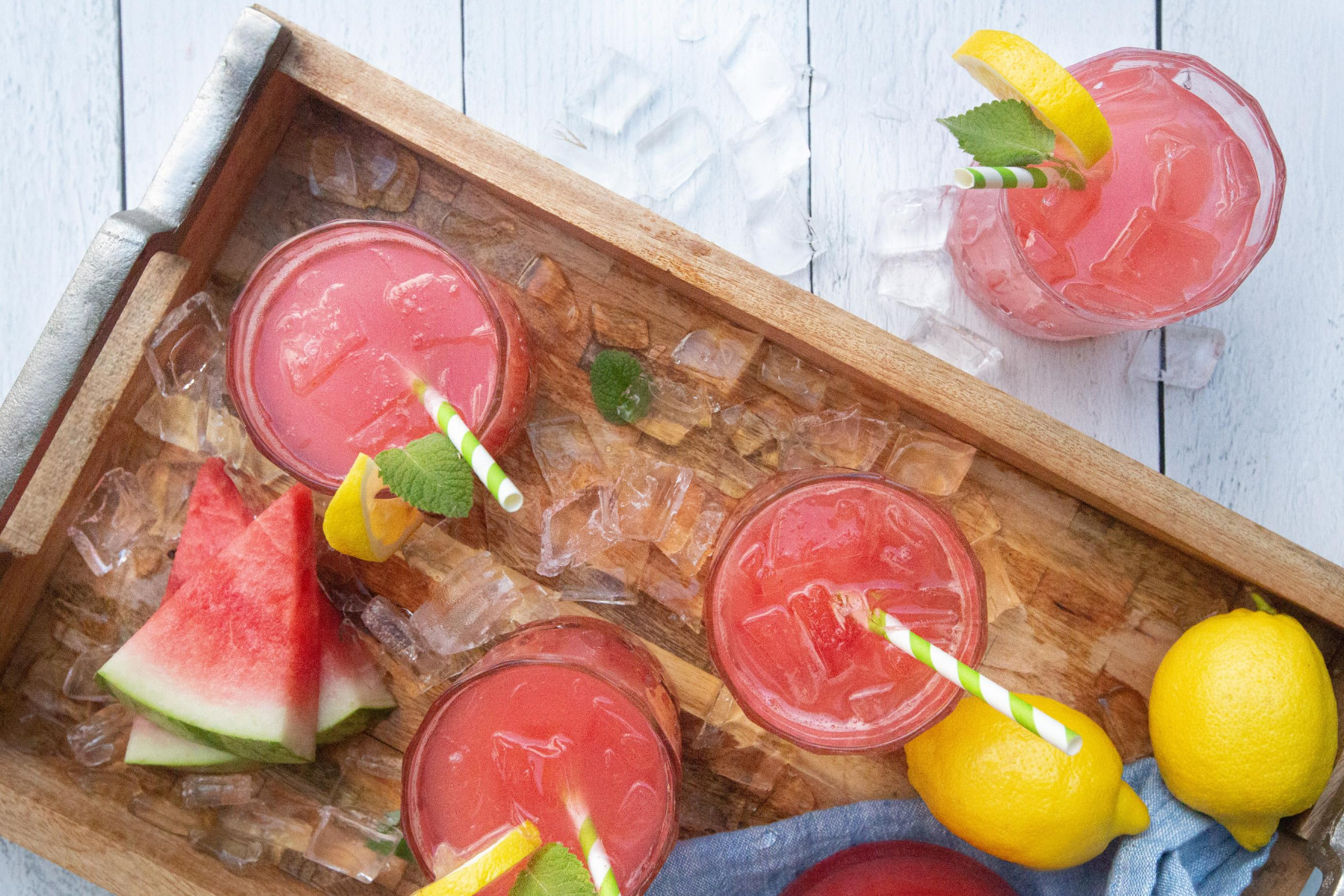 Glasses of watermelon lemonade, watermelon slices and lemons on a wooden tray.