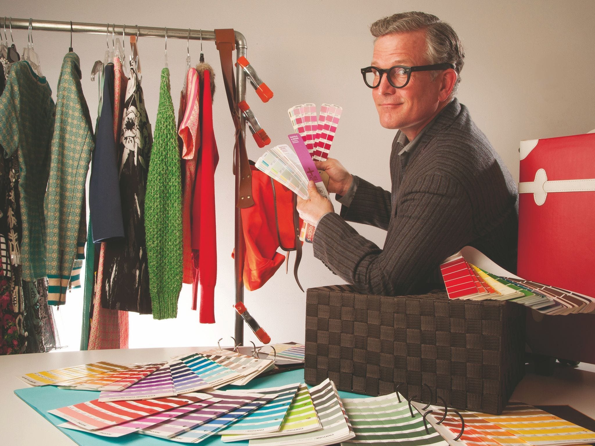 A man looks through color swatches while searching through women's clothing.