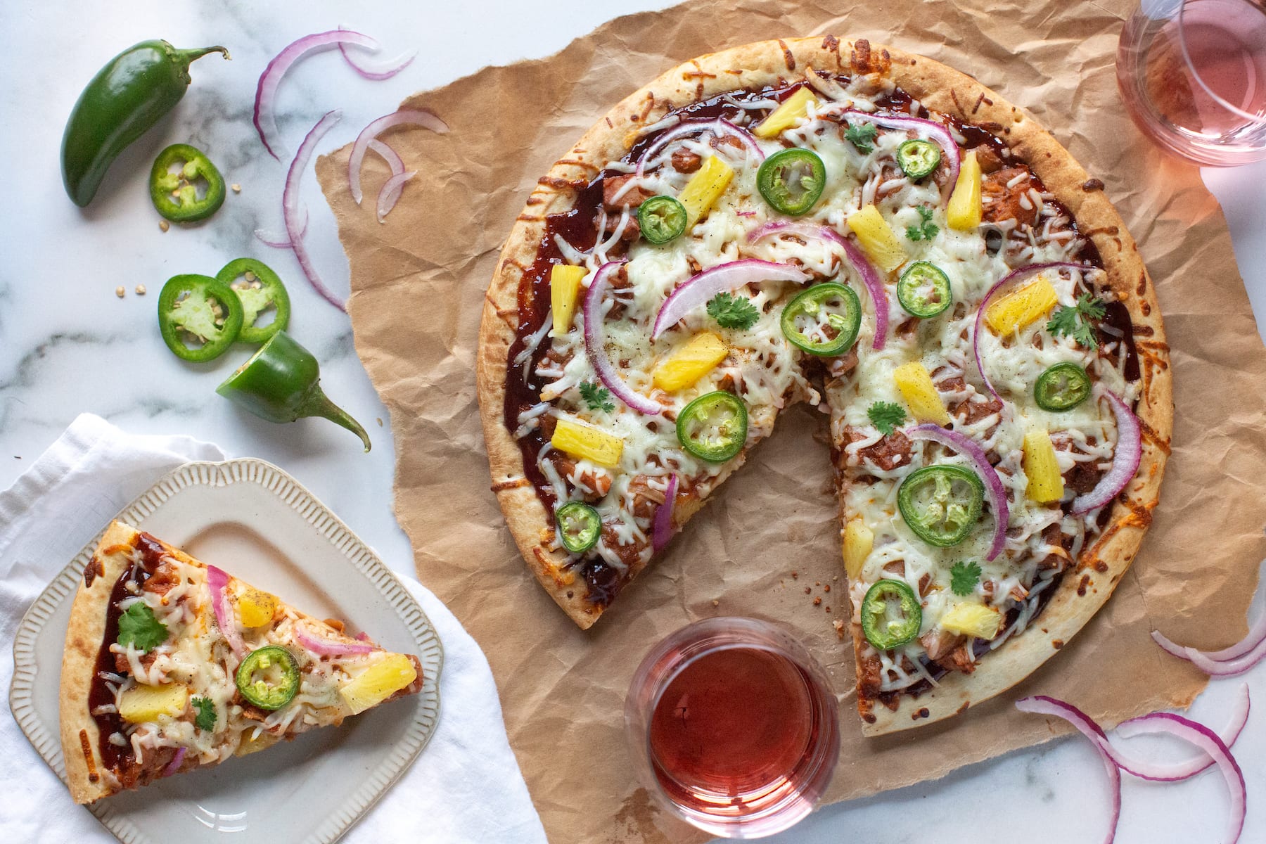 Image Picture of a pizza topped with barbecue sauce, plant-based meat substitute jackfruit, vegan mozzarella, sliced jalapeños, pineapples chunks, and sliced red onion