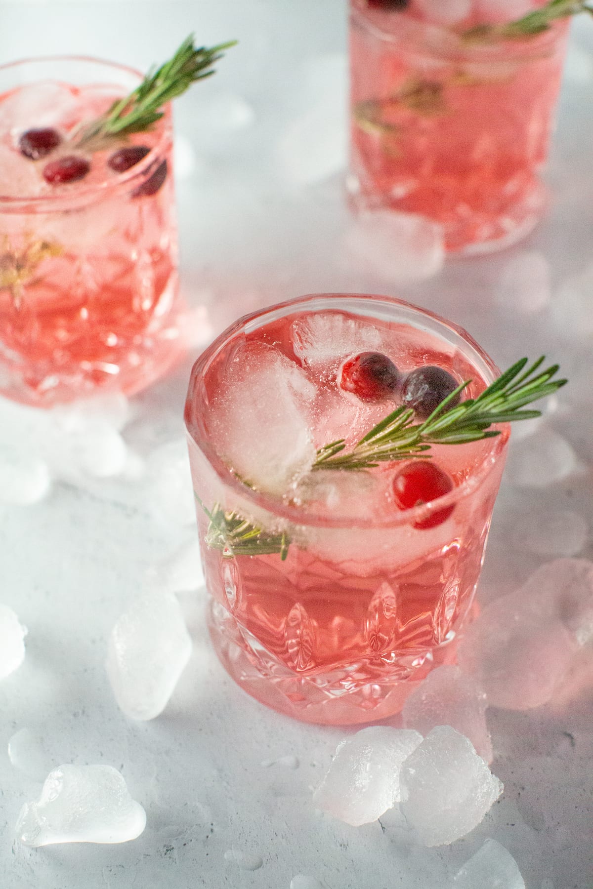 Several Sparkling Cranberry Ginger Rosemary Mocktails sit in the light, surrounded by ice.