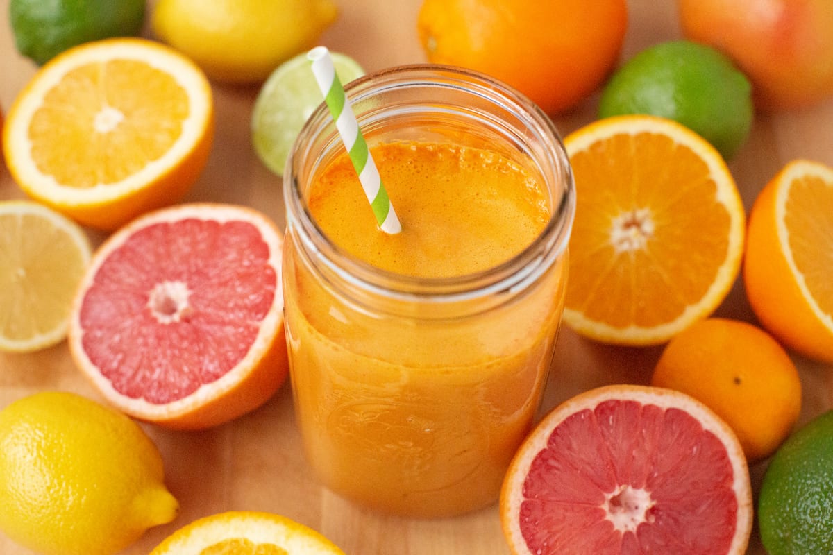 A Mason jar full of fresh-squeeze citrus juice sits on a cutting board strewn with more than a dozen halves of additional citrus fruits.