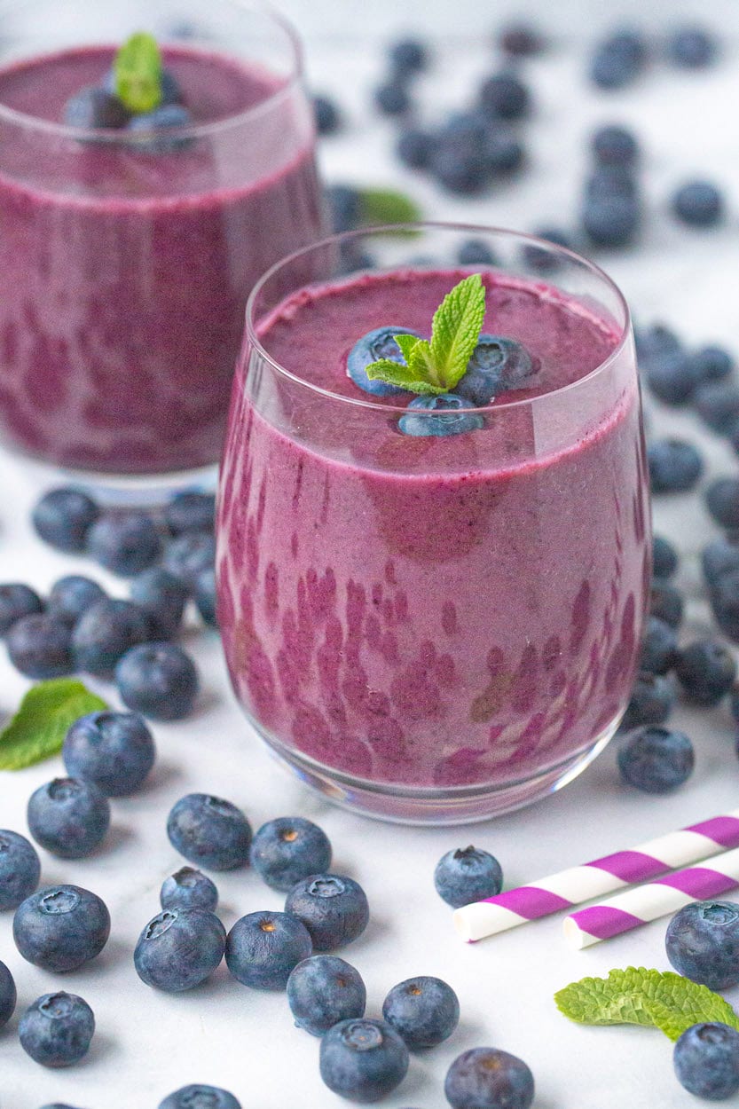 Two ready-to-enjoy Banana Blueberry Smoothies sit in the middle of hundreds of fresh blueberries.