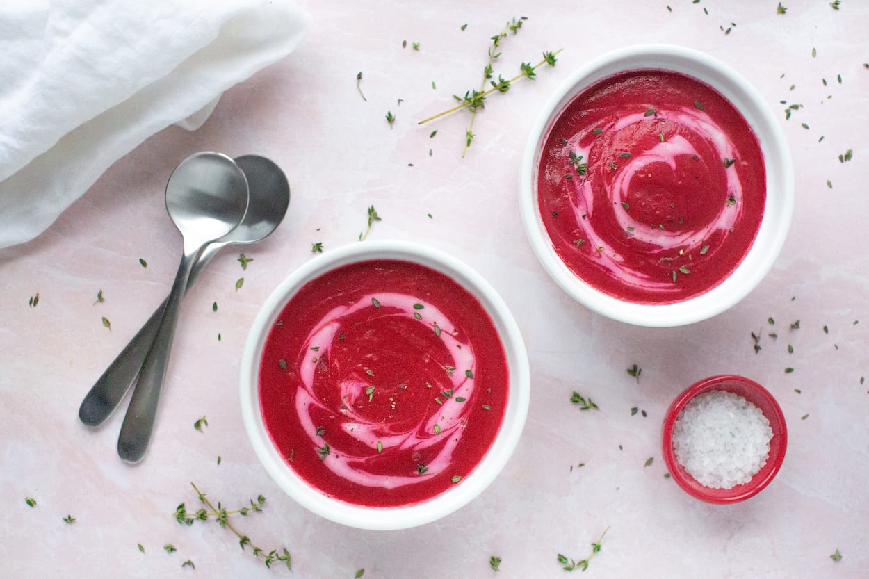 Two bowls of rich, earth beetroot soup, swirled with cashew cream and sprinkled with fresh thyme leaves.